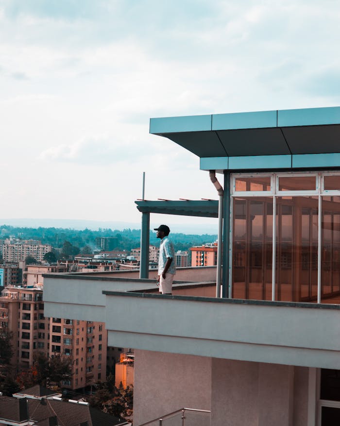 pexels-photo-1725385-1 Man standing on a modern balcony overlooking a city skyline on a bright day.